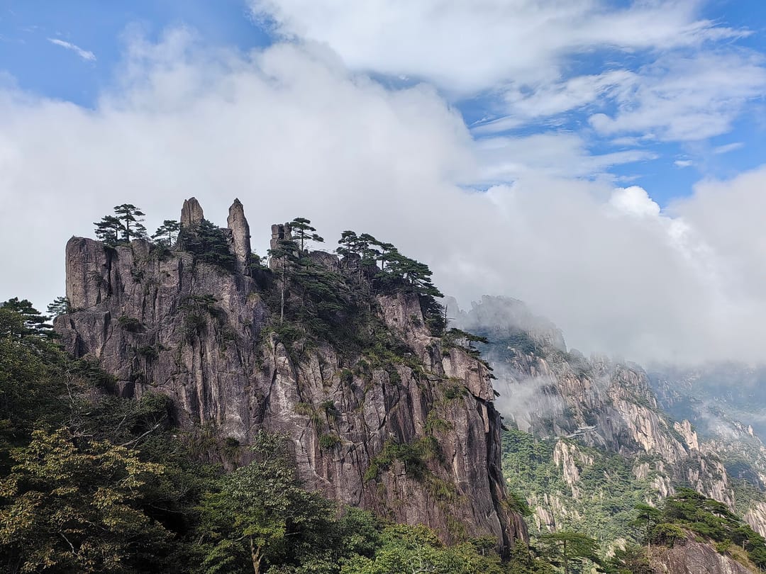 Pitons de granit de Huangshan couverts de pins, avec des nuages qui débordent la crête à l'arrière-plan