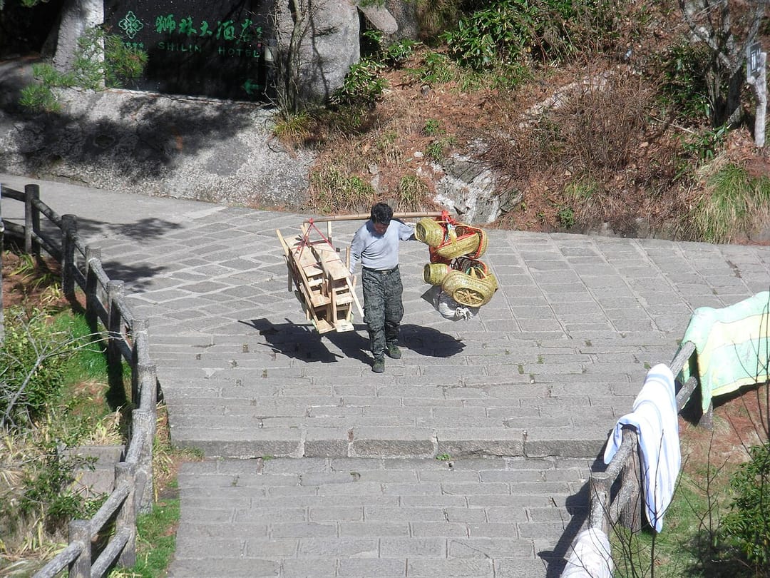 Un porteur monte des escaliers de pierre à Huangshan, palanche sur l'épaule chargée d'un cadre en bois et de paniers tressés