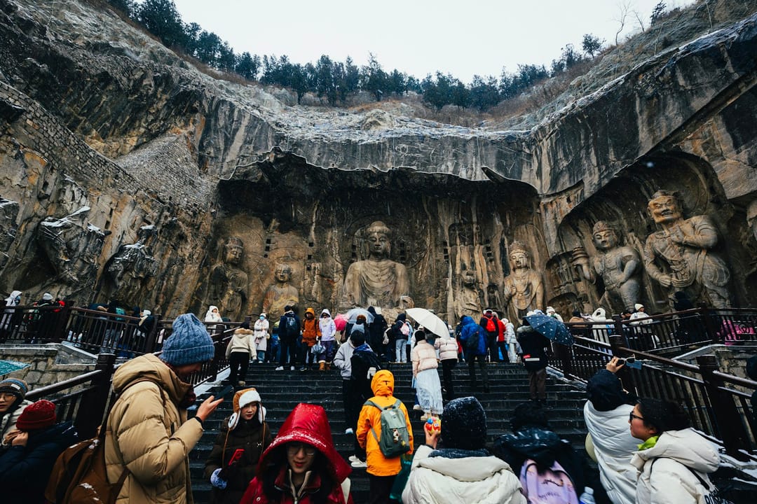 La grotte de Fengxian aux grottes de Longmen : le bouddha Vairocana assis au centre de la falaise, entouré de disciples, de bodhisattvas et de gardiens sculptés, avec un escalier de visiteurs sous la neige