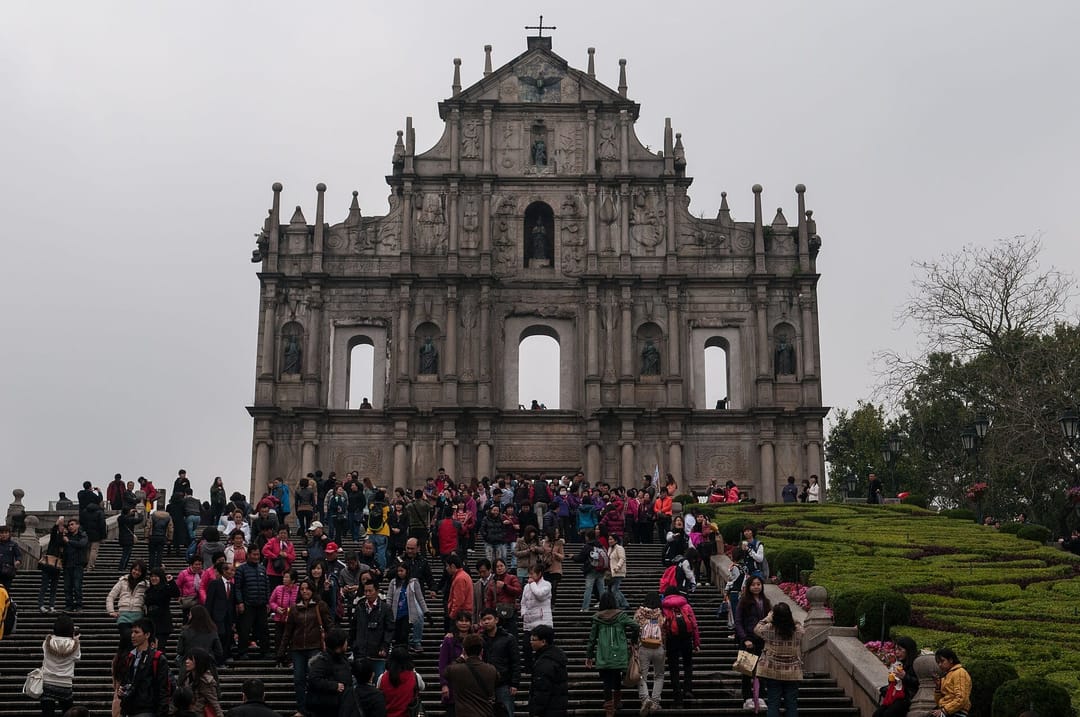 La façade baroque des ruines de l'église Saint-Paul à Macao, seul mur restant orné de statues et de bas-reliefs, surmontée d'une croix, au sommet d'un grand escalier de pierre couvert de visiteurs