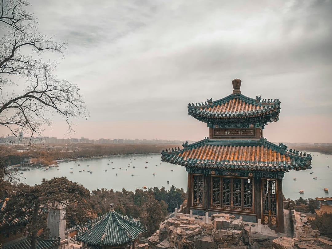 Le lac Kunming du Palais d'Été de Pékin couvert de barques de promenade, vu depuis la colline de la Longévité, avec un pavillon à double toiture de tuiles vernissées au premier plan