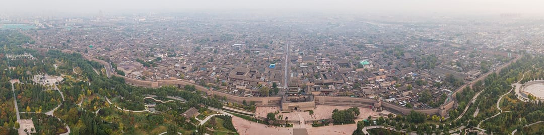 Vue aérienne de Pingyao : le rempart et sa tour de porte au premier plan, la trame serrée des maisons à cour derrière, la ville moderne au fond
