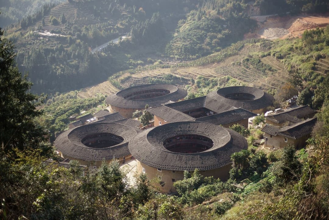 L'ensemble de tulou de Tianluokeng vu depuis la hauteur : quatre bâtiments circulaires en terre crue à toit de tuiles grises disposés autour d'un cinquième bâtiment carré, au milieu de collines cultivées en terrasses